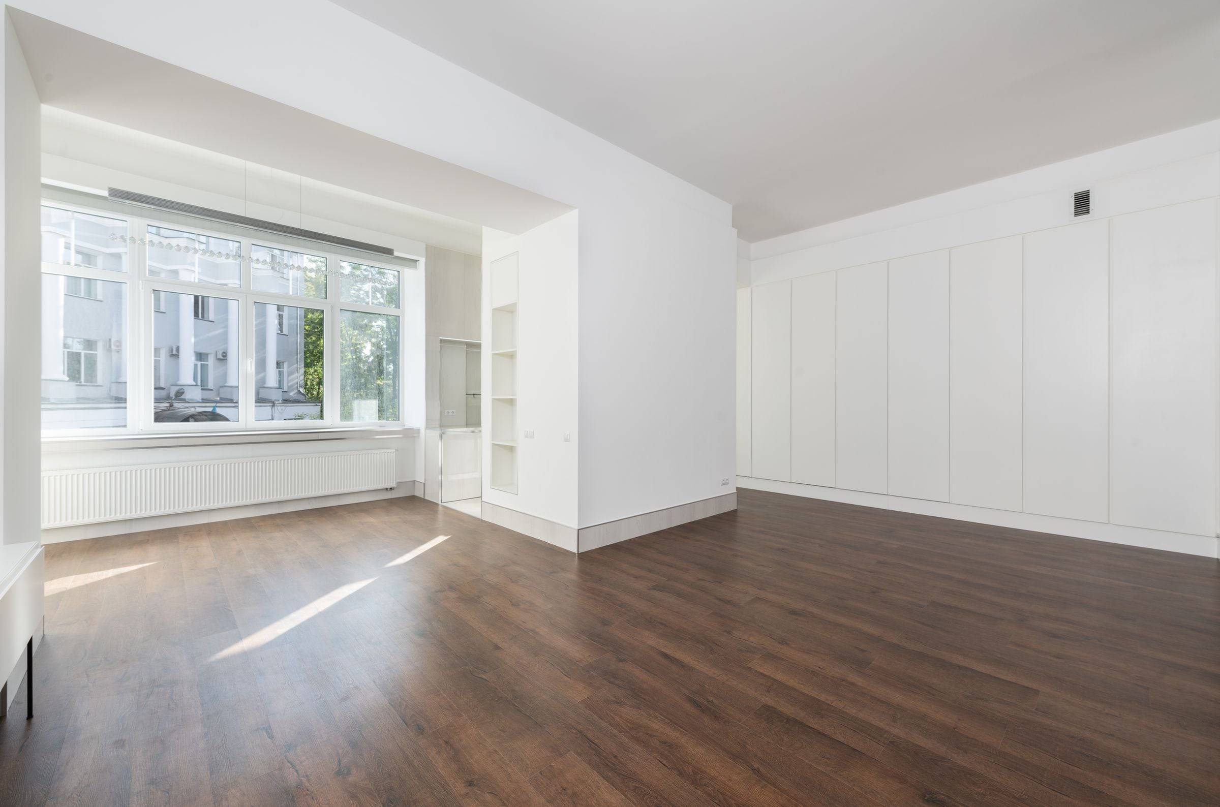 Appartement vide et lumineux entre deux locataires, armoires murales blanches et parquet foncé.