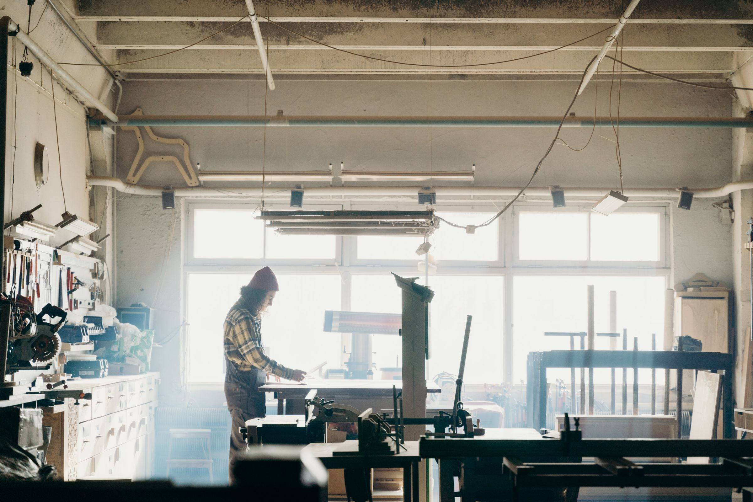 Atelier lumineux aux grandes fenêtres, une menuisière à l’établi au milieu des machines.