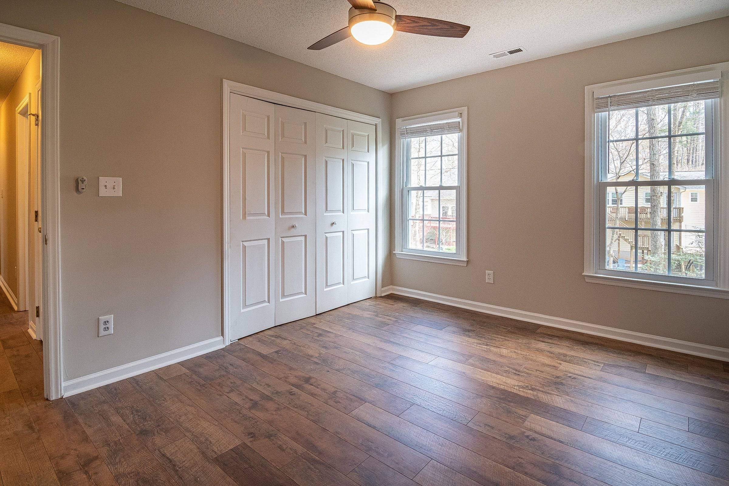 Chambre vide avec des portes de placard pliantes fatiguées, murs beiges et parquet foncé.