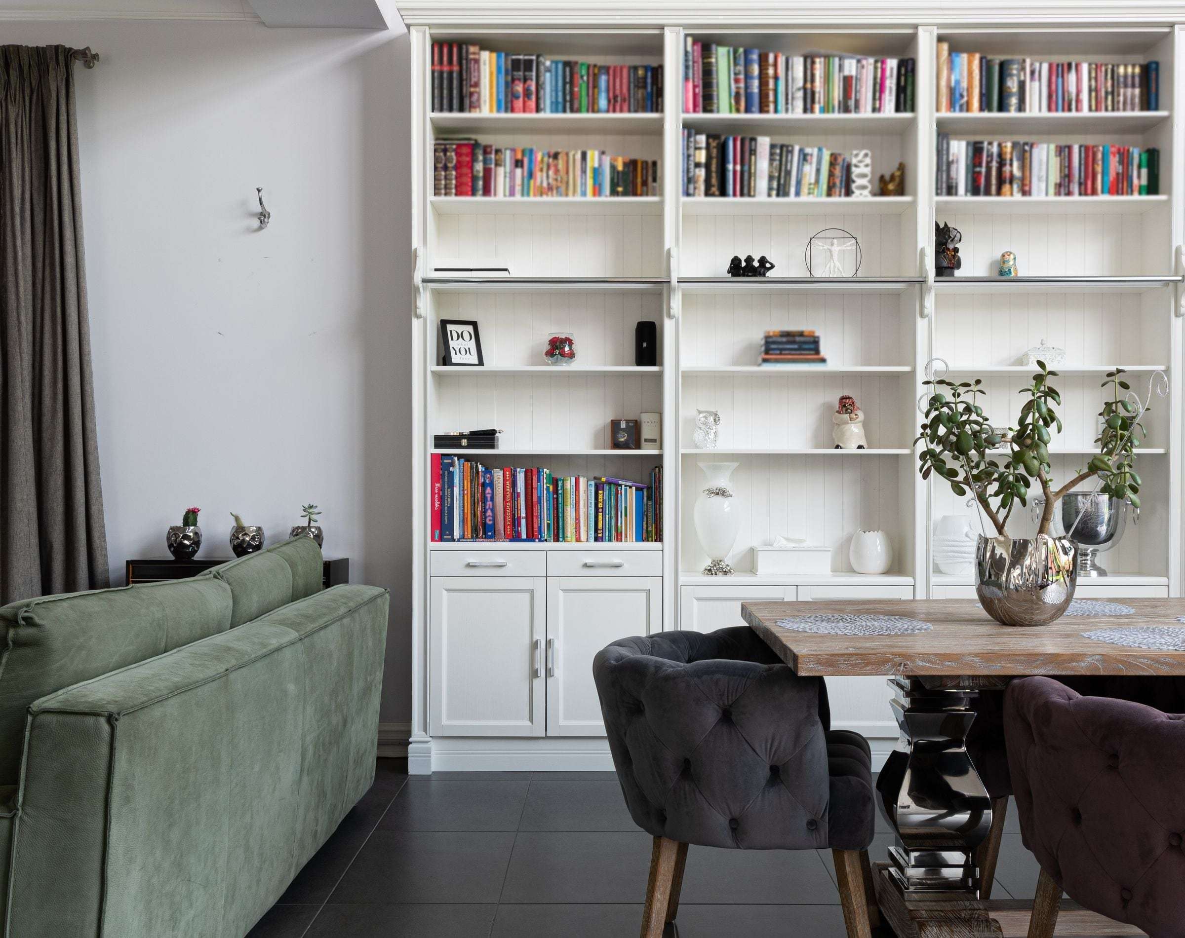 Bibliothèque blanche toute largeur remplie de livres, tablettes sur crémaillère et portes basses.