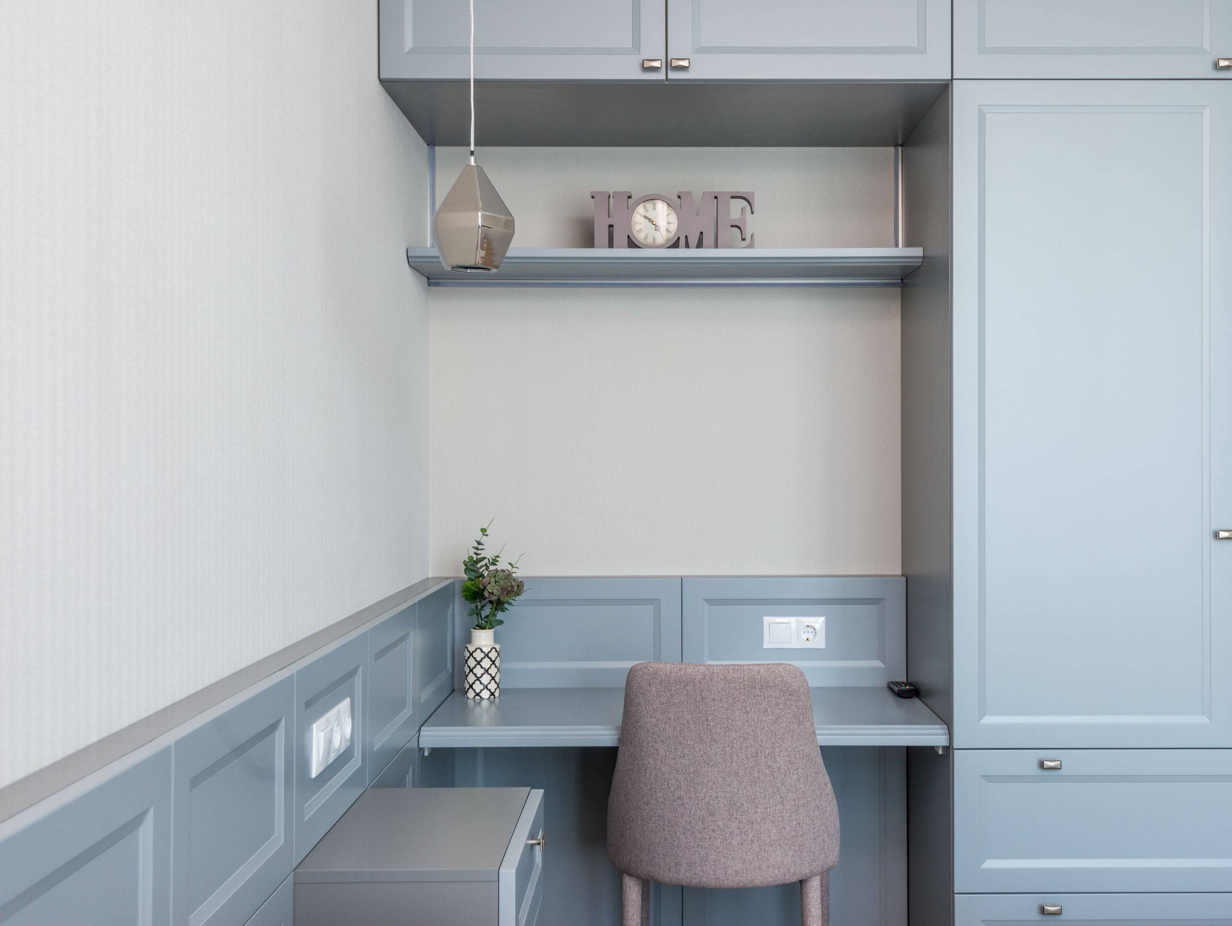 Niche de bureau intégrée entre des armoires gris-bleu, plan de travail, chaise et tablette avec horloge.
