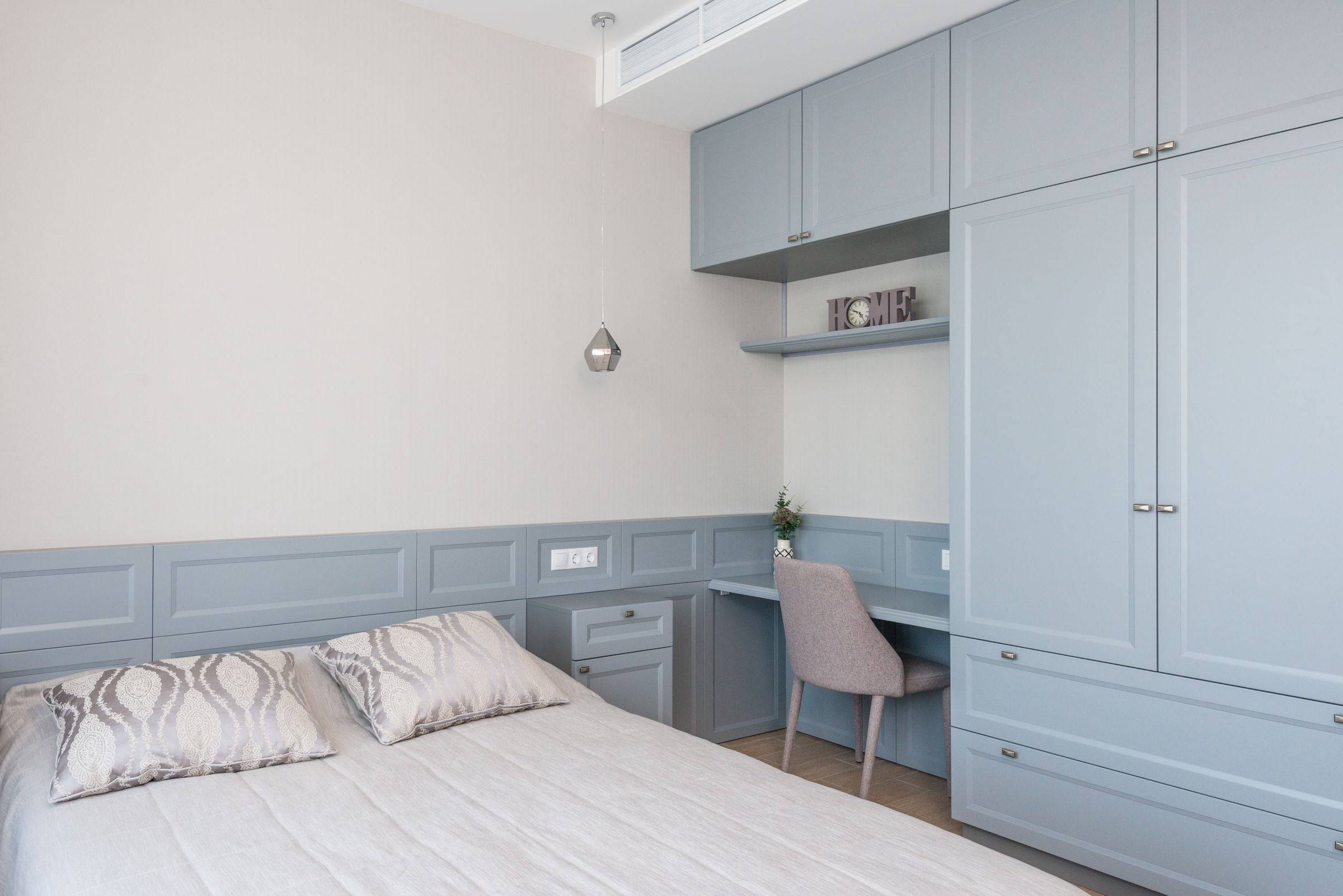 Chambre avec armoire murale gris-bleu toute hauteur, bureau intégré et lambris bas assorti.