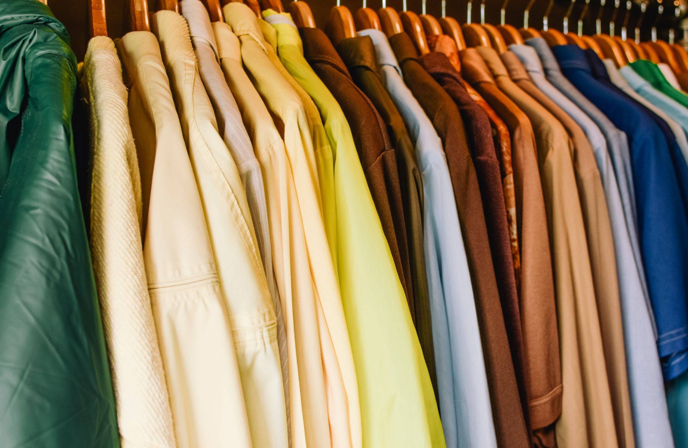 Penderie pleine de chemises et de vestes de toutes les couleurs sur des cintres en bois.